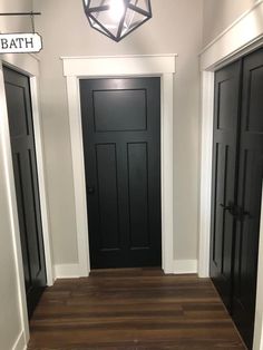 an empty hallway with black doors and wood flooring in the center is lit by a light fixture