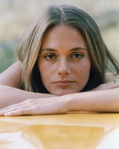 a woman leaning on the hood of a yellow car with her arms folded over her head