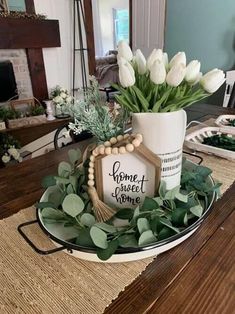 white tulips and greenery in a vase on a table with a sign that says home sweet home