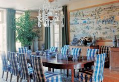 a dining room table with blue and white striped chairs, chandelier and painting on the wall