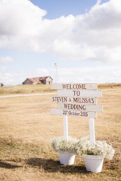 a welcome sign in the middle of a field with two buckets full of flowers