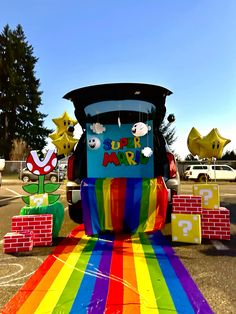 a colorful train is parked in the parking lot next to some fake bricks and trees