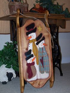 a wooden sign with two snowmen and a dog on the ground in front of a table