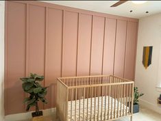 a baby's crib in front of a pink wall with horizontal paneling