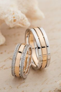 two gold wedding bands with diamonds on them next to a seashell and starfish