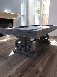 a pool table in the middle of a living room with wood flooring and white walls