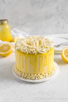 a yellow cake with white frosting and lemons around it on a plate next to some forks