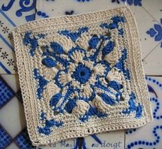 a crocheted square with blue and white flowers on it sitting on a tile floor