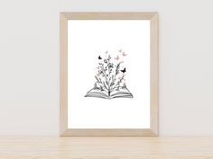 an open book with flowers and butterflies on it sitting on a table next to a wooden frame