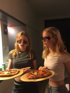 two women are holding pizzas in their hands