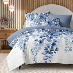 a bed with blue and white flowers on the comforter, pillows and pillow cases