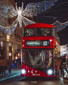 a red double decker bus driving down a street with christmas lights on the side of it