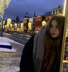 a woman standing on the side of a street next to a pole with lights hanging from it