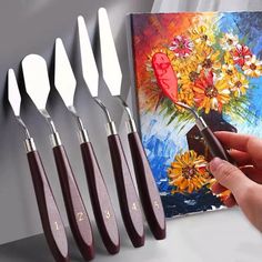 a person holding a knife in front of six knives on a table next to a painting