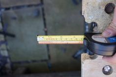 a person holding a pair of scissors and measuring the length of a piece of wood