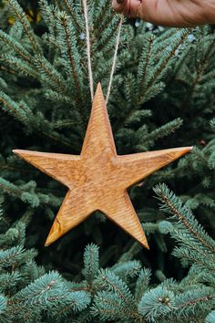 a wooden star ornament hanging from a christmas tree in someone's hand