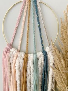 several different colors of yarn hanging on a circular wall decoration with gold hoop and plant