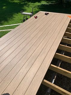 a wooden deck is being built in the yard with tools on it and some grass