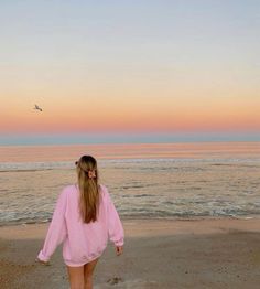 a girl walking on the beach at sunset with her back to the camera, facing the ocean