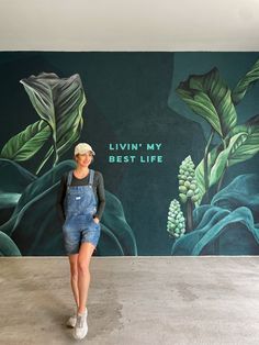 a woman standing in front of a wall with plants painted on it and the words livin'my best life