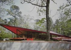 a large red triangular structure in the middle of a forest with trees and benches around it