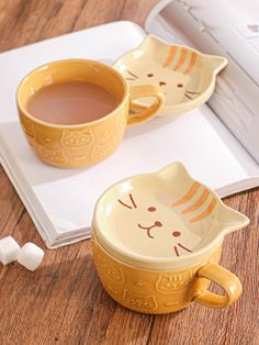 two yellow mugs sitting on top of a book next to marshmallows