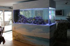 a fish tank filled with purple flowers sitting on top of a wooden floor next to a dining room table