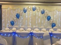 the table is set up with blue and white balloons, silver plates and napkins