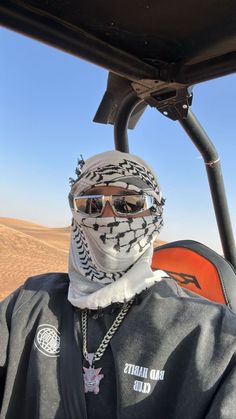 a man wearing sunglasses and a bandana sits in a buggy on the desert