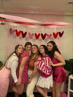 four women pose for a photo in front of a backdrop with hearts and streamers