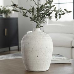 a white vase sitting on top of a wooden table next to a book and plant