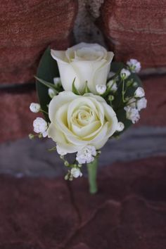 a white rose and baby's breath boutonniere on a brick wall