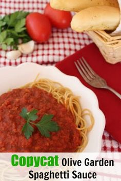 a bowl of spaghetti sauce on a red and white checkered table cloth next to bread, tomatoes, garlic, parsley