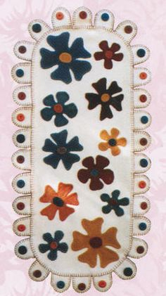 an embroidered piece with flowers on it is hanging from a pink wallpapered background