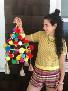 a woman holding up a multicolored mobile with pom poms on it