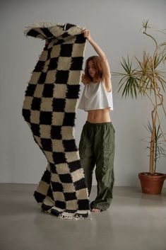 a woman standing next to a giant black and white rug on the floor in front of a potted plant