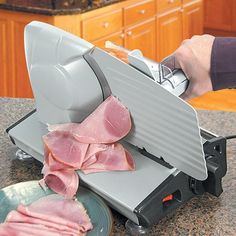 a person using a meat slicer to cut up ham on a counter with other food items