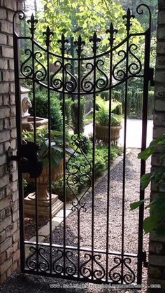 an iron gate in front of a brick wall with potted plants on the other side