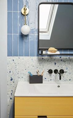 a bathroom with blue and yellow tiles on the wall, sink and mirror above it