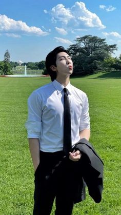 a man in a white shirt and black tie standing on the grass with his eyes closed