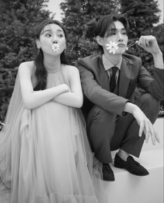 a man and woman sitting next to each other in front of some trees with flowers on their mouths