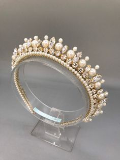 a tiara with pearls and crystal stones on it's headband, sitting on a clear acrylic stand