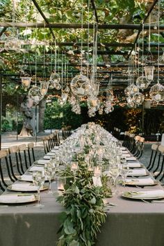 an outdoor dining table set with place settings and hanging glass globe chandeliers over it