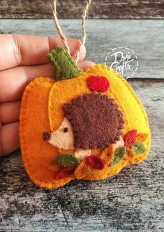 a hand is holding a small felt pumpkin ornament with a hedge on it