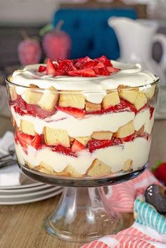 a cake with strawberries and cream on top is sitting on a glass plate next to plates