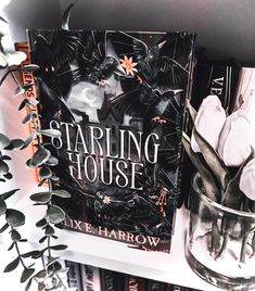 a book sitting on top of a shelf next to a glass vase filled with flowers