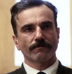 a man with a moustache wearing a suit and tie looking at the camera