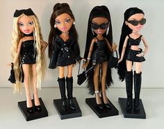 four dolls are dressed up in black outfits and boots, one is wearing cat - eye glasses