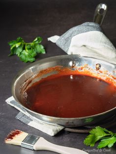 a sauce pan with red liquid and garnish on the side next to a spatula