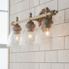 a bathroom light fixture with five clear glass shades hanging from it's side on a white tiled wall